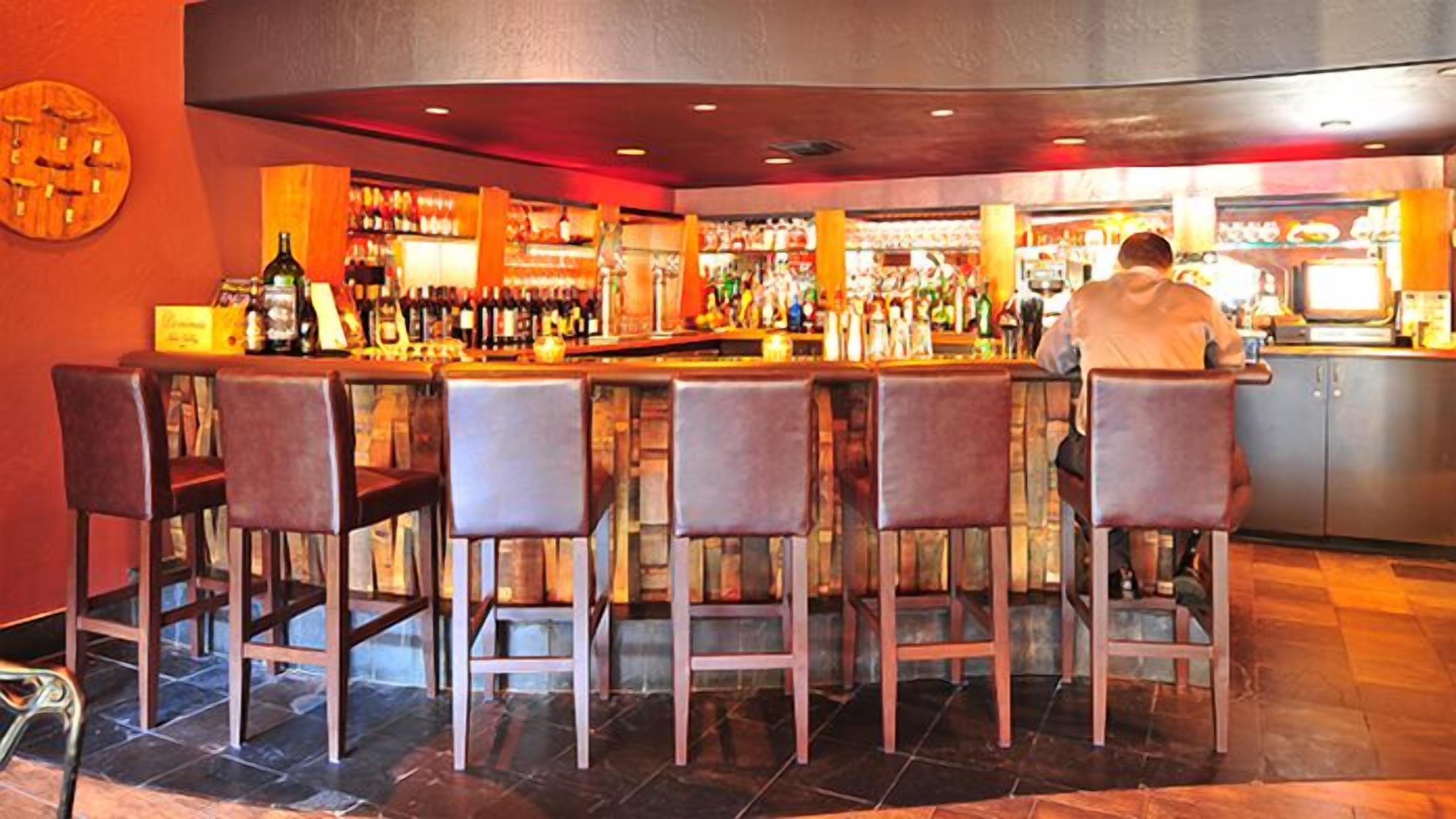 A bar area with a counter, multiple stools, and a variety of bottles and glasses.