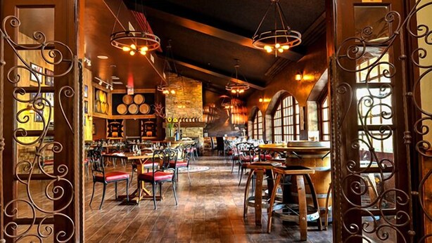 A spacious restaurant with high ceilings, exposed brick walls, and large windows.