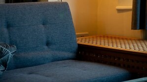 Een kamer met een blauwe bank, een houten lamp met een enkele lamp en een kamerkleed met een patroon.