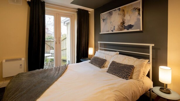 Een slaapkamer met een bed, een nachtkastje met een lamp, een radiator en een raam met gordijnen.