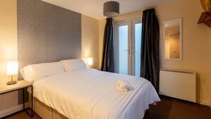 A hotel room with a bed, bedside lamps, a window with curtains, a radiator, and a wall-mounted mirror.