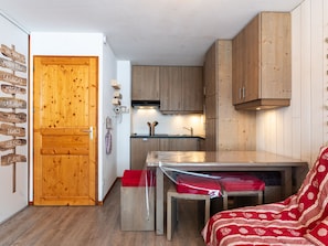 A compact kitchen with wooden cabinets, a built-in oven, and a small dining area with a table and bench.