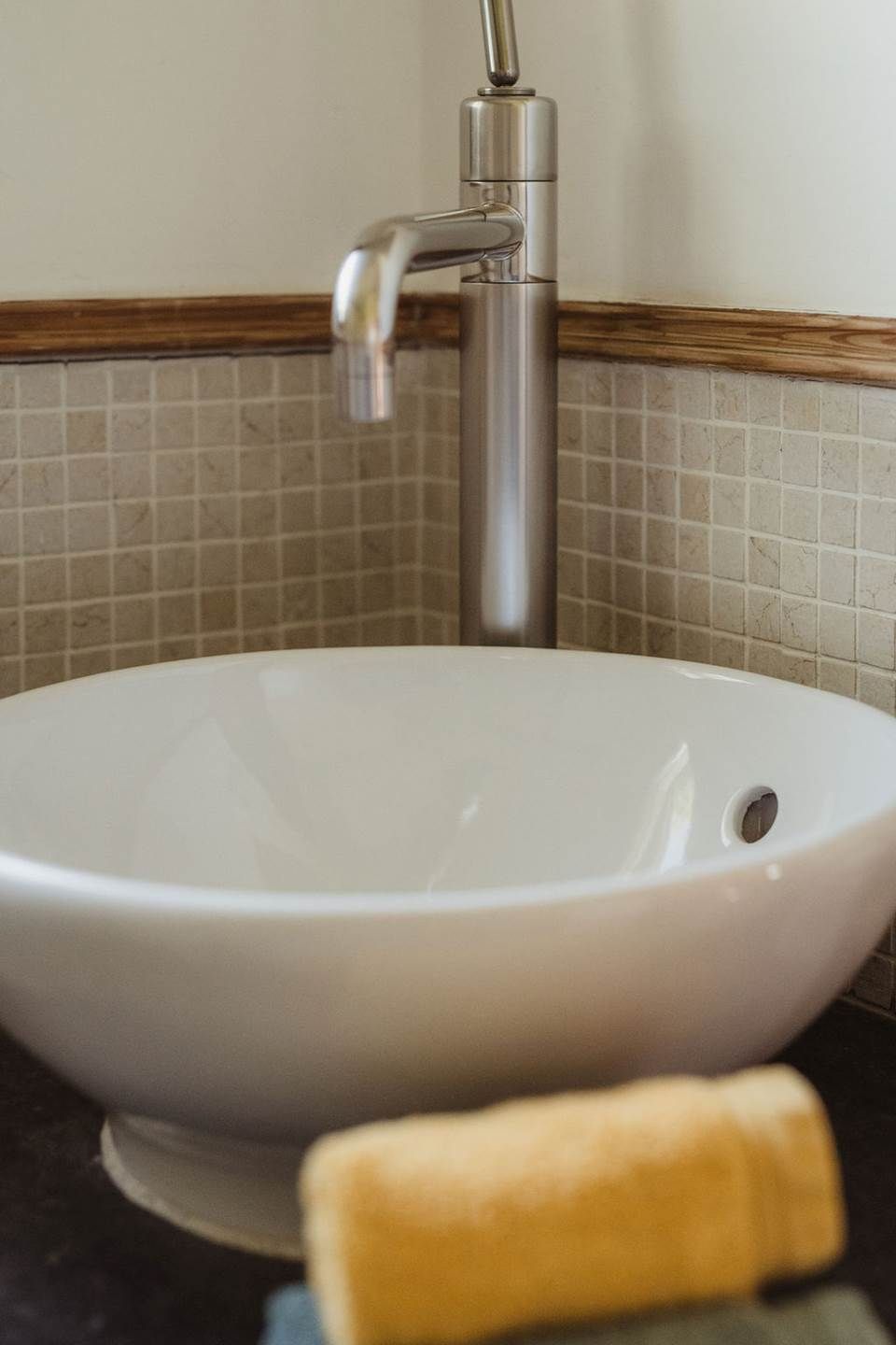 Et badeværelse med en hvid vask, en kromarmatur og et flisebeklædt backsplash.