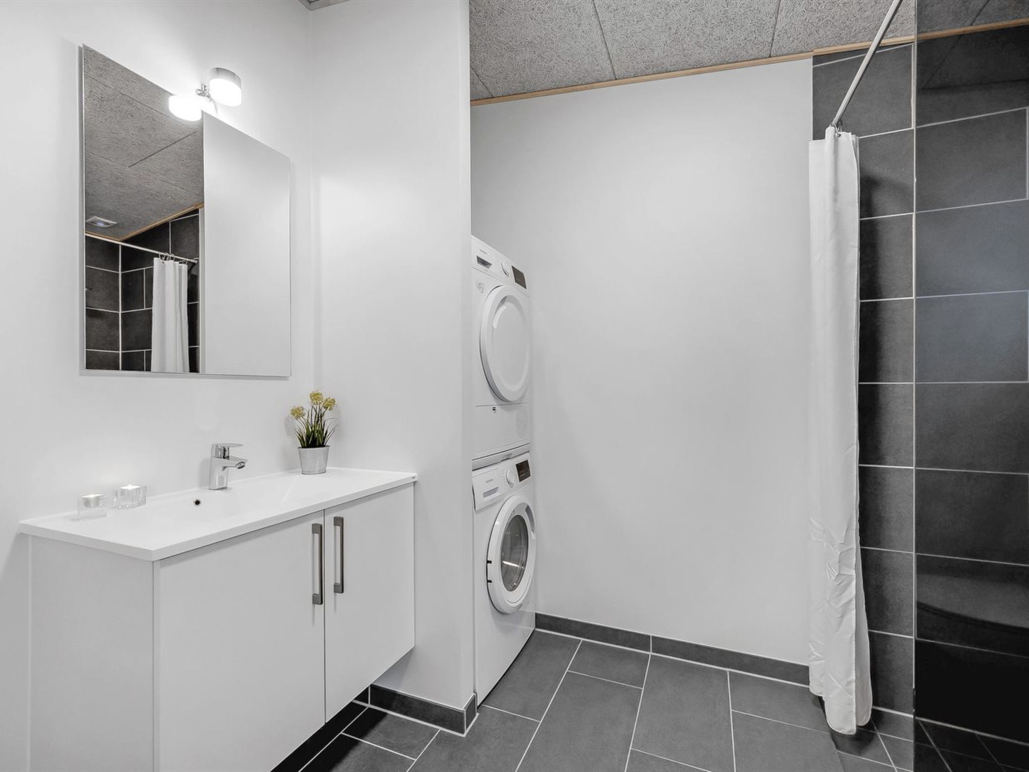 Ein modernes Badezimmer mit Waschbecken, Spiegel und Waschmaschine in Weiß.