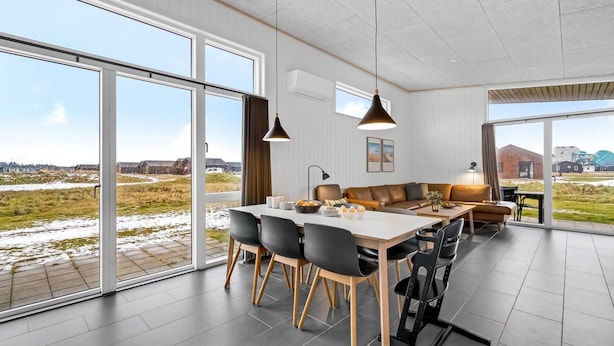 Uma sala de jantar ampla, com uma mesa grande e cadeiras, um sofá e vista para o exterior.
