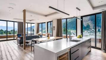 Une cuisine moderne dotée d’un grand îlot central, d’un coin repas et de grandes fenêtres offrant une vue sur les montagnes.