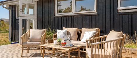 A wooden deck with outdoor furniture, including chairs and a table, in front of a building with large windows.