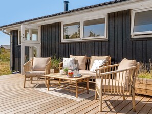 A wooden deck with outdoor furniture, including chairs and a table, in front of a building with large windows. - "Zina" - 600m from the sea by Interhome (Hjørring)