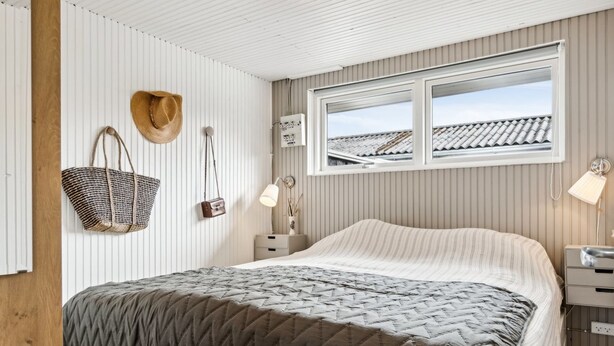 A bedroom with a bed, a window, a nightstand, a lamp, and a wall-mounted hat and bag.