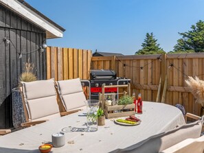 An outdoor dining area with a table set for two, a barbecue grill, and a wooden fence in the background.