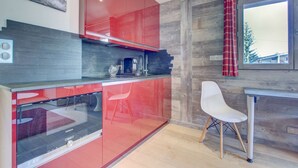Una cocina moderna con armarios rojos, horno integrado y ventana con cortina roja.