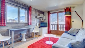 Una sala de estar moderna con un sofá gris, una mesa de centro blanca, un tapete rojo, un televisor y una pared de acento de madera.
