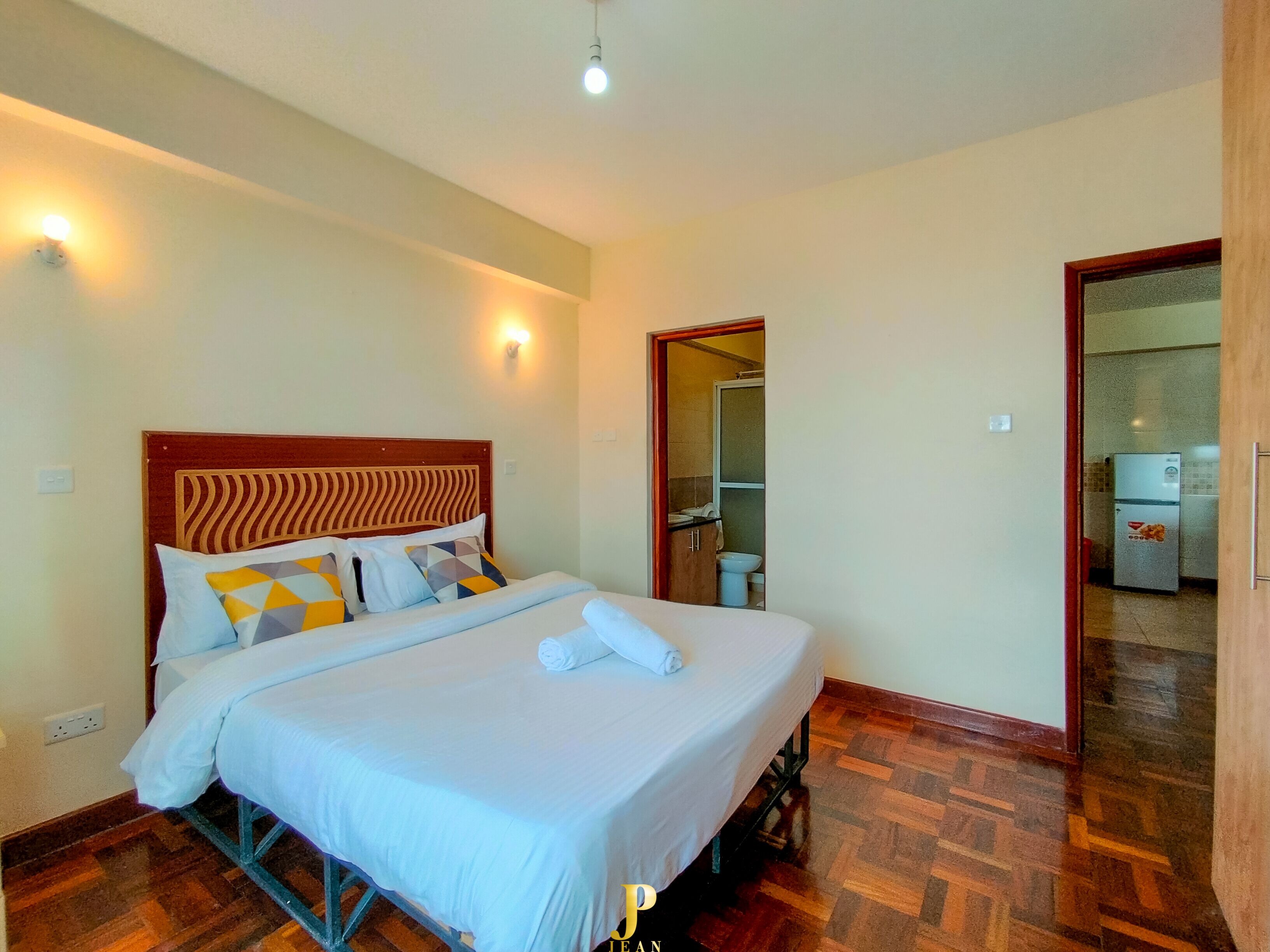 A hotel room with a bed, a wooden headboard, a wall-mounted light, and a door leading to a bathroom.