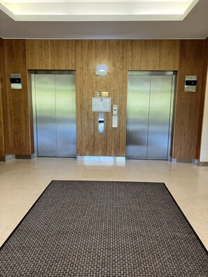 A modern elevator area with two elevators, a wooden panel wall, and a textured floor mat. - City Escape Mounts Bay Apartment. Near Kings Park -  Parking - Wifi (Perth)
