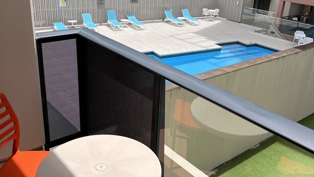 Een balkon met een zwembad, blauwe ligbedden en een tafel.
