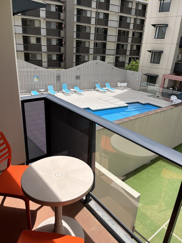 Un balcon avec une piscine, des fauteuils de jardin bleus et une table.