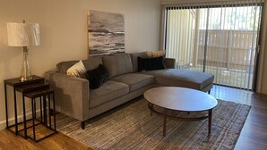 A living room with a grey sectional sofa, a round coffee table, a floor lamp, and a painting on the wall. - Modesto 2 Bdrm/2 Ba unit in gated area nr shopping, eateries, in unit wash/dryer (Modesto)