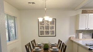 A dining room with a wooden table set for four, surrounded by chairs. A chandelier hangs above the table, and a framed artwork is on the wall. - Modesto 2 Bdrm/2 Ba unit in gated area nr shopping, eateries, in unit wash/dryer (Modesto)
