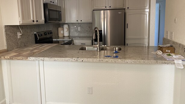 A kitchen with white cabinets, stainless steel appliances, a granite countertop, and a blue door in the background. - Modesto 2 Bdrm/2 Ba unit in gated area nr shopping, eateries, in unit wash/dryer (Modesto)