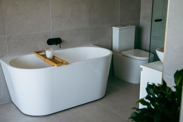 Een moderne badkamer met een vrijstaand bad, toilet en een douchecabine met glazen wanden.