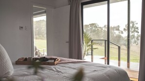 Ein Schlafzimmer mit einem großen Bett, einem Holztablett mit Gegenständen und Blick auf eine Terrasse und Bäume durch eine Glastür.