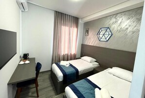 Een hotelkamer met twee bedden, een bureau, een stoel en een groot raam met gordijnen.