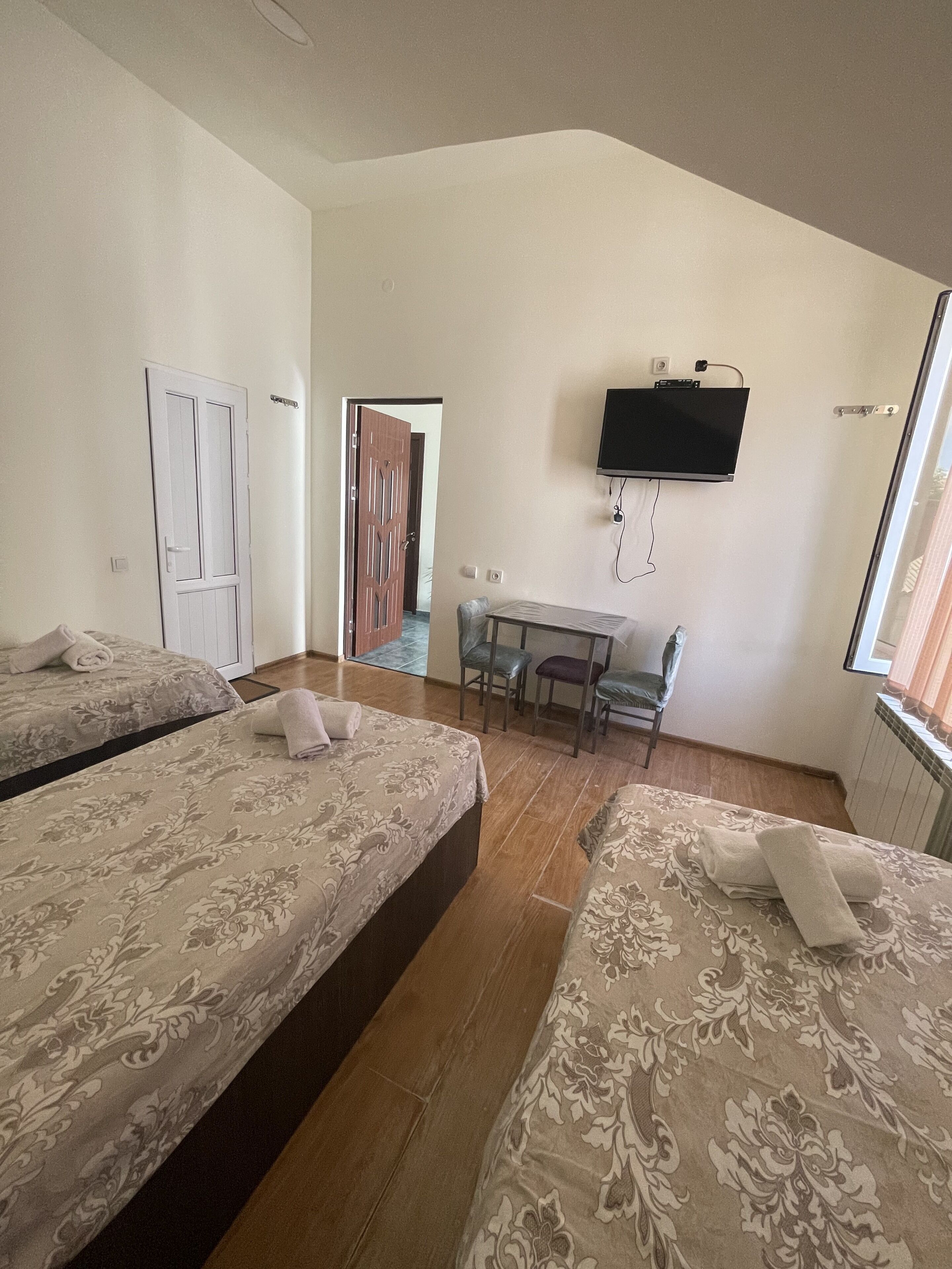 A hotel room with two beds, a desk, a chair, a television, and a window.