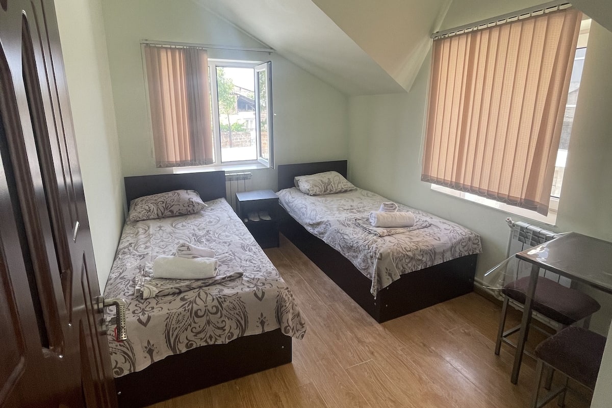 Une chambre avec deux lits, une petite table et une fenêtre avec des rideaux.