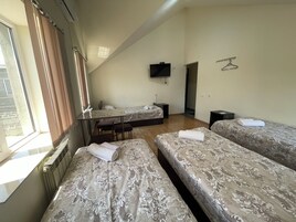 Een hotelkamer met twee bedden, een klein tafeltje, een aan de muur bevestigde televisie en een raam met gordijnen.