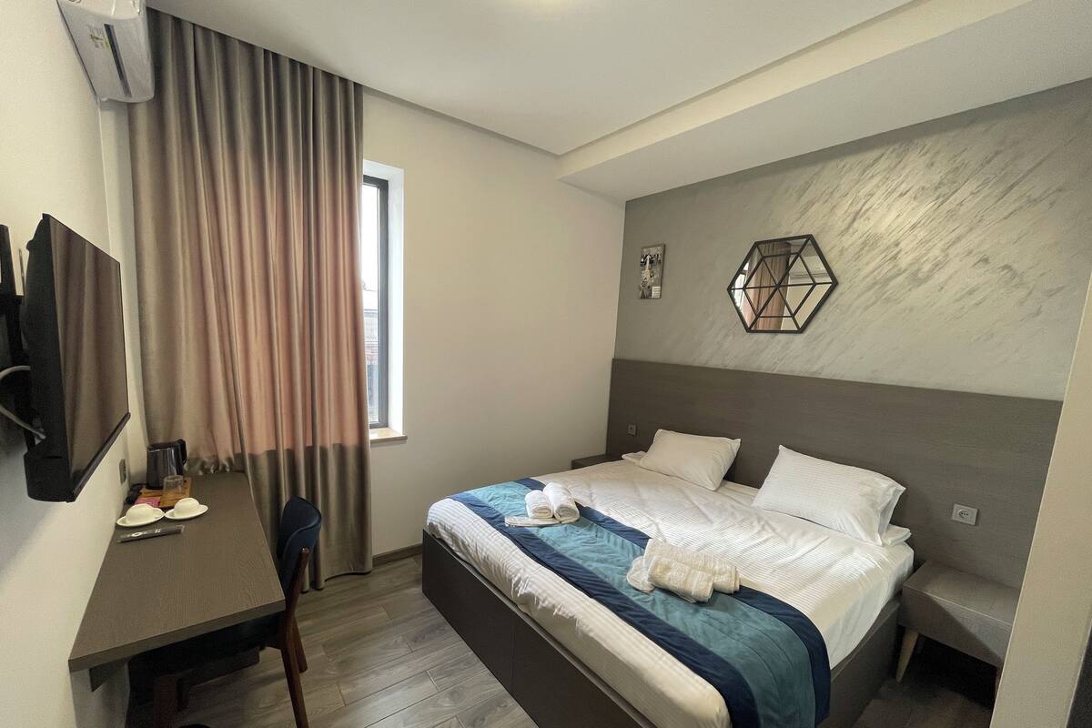 Une chambre d’hôtel équipée d’un lit, d’un bureau, d’une chaise, d’une télévision et d’une fenêtre avec des rideaux.