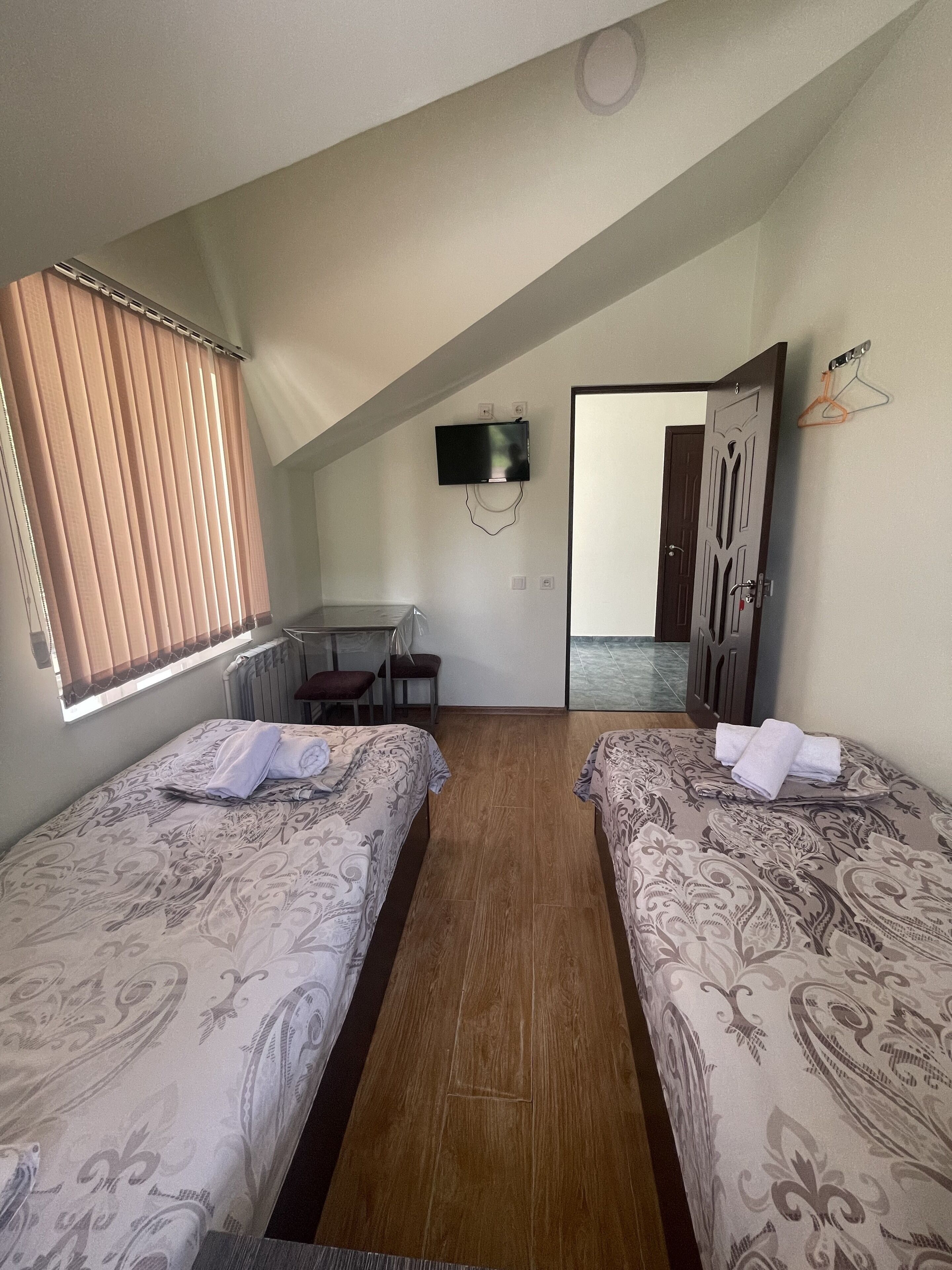 A room with two beds, a desk, a TV mounted on the wall, and a door leading to another room.