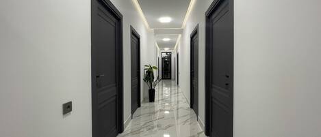 A modern hallway with marble flooring, dark doors, and recessed lighting.