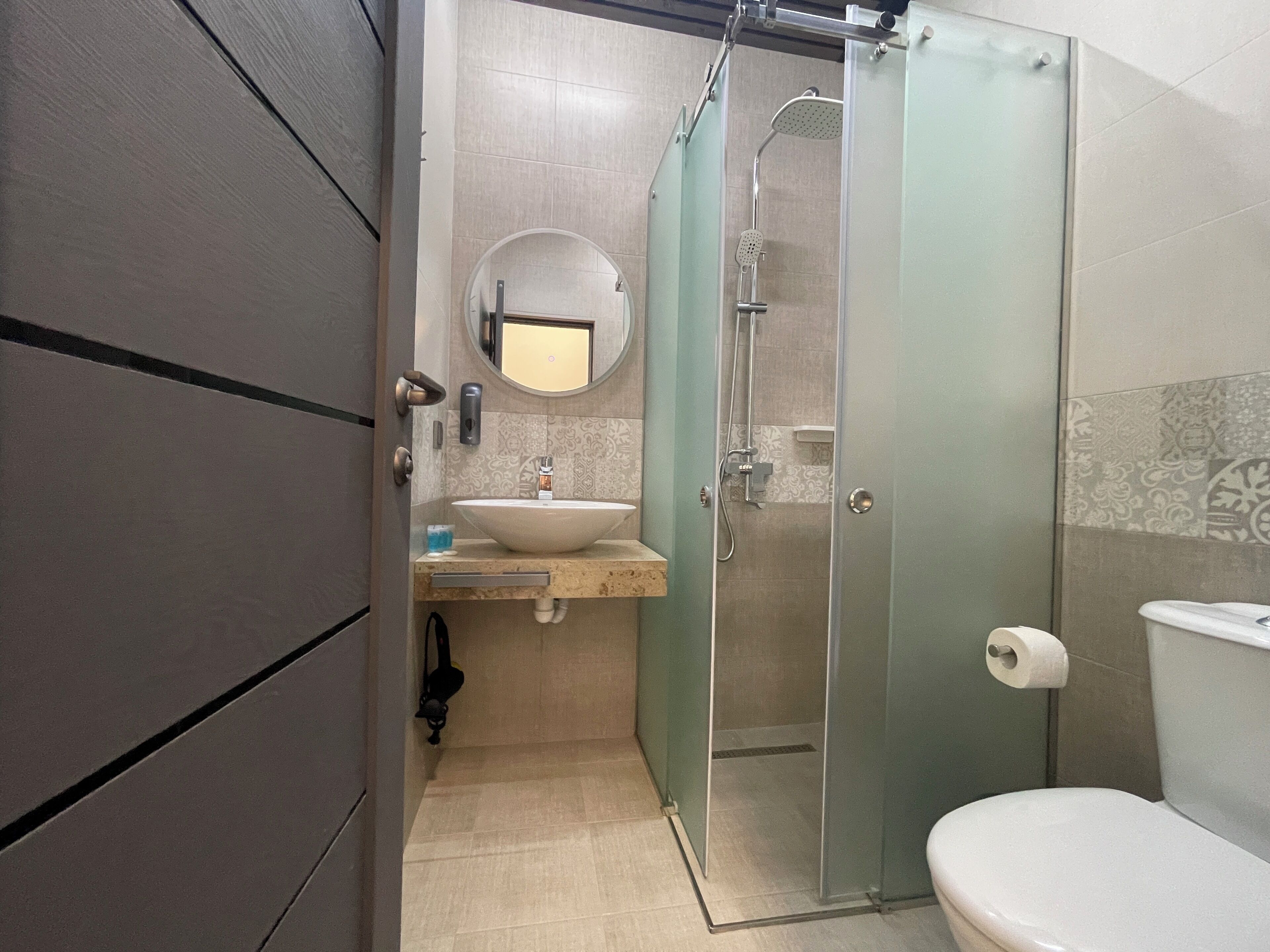 Ein Badezimmer mit einer Duschkabine, einem Waschbecken inklusive Spiegel und einer Toilette.