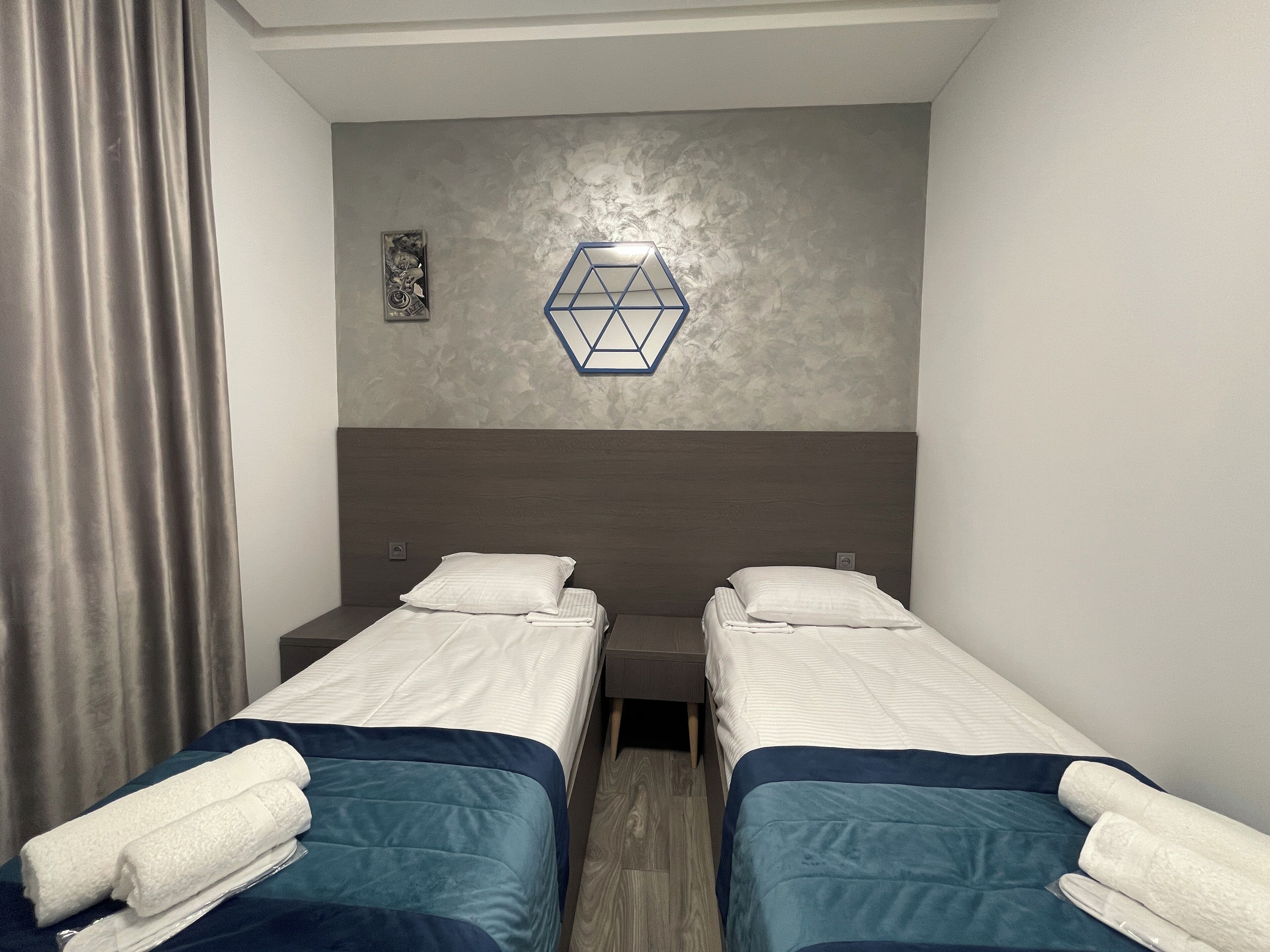 A hotel room with two single beds, a grey textured wall, a geometric light fixture, and a wooden floor.