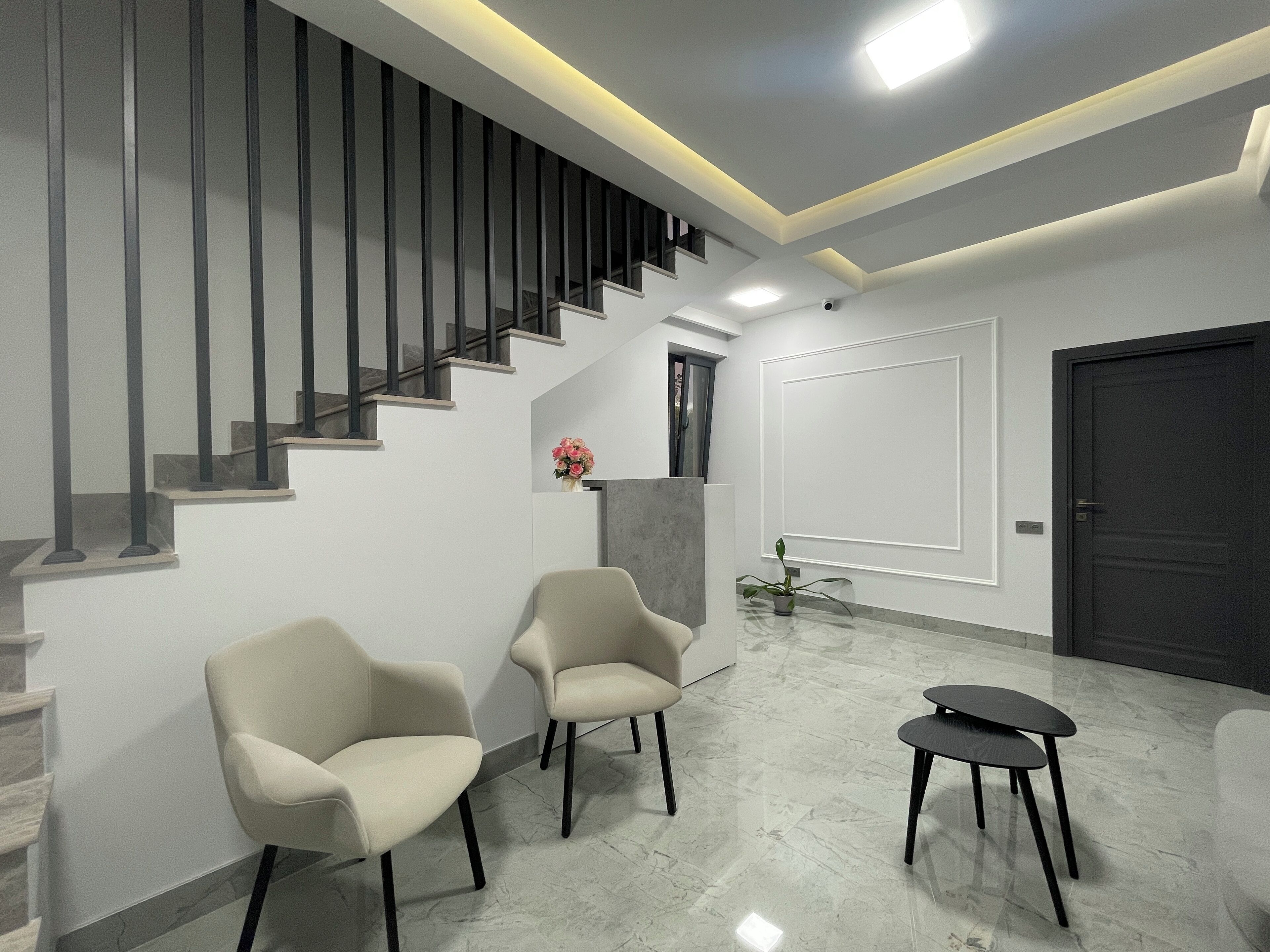Un interior moderno con una escalera, dos sillones, una mesita y una puerta oscura.