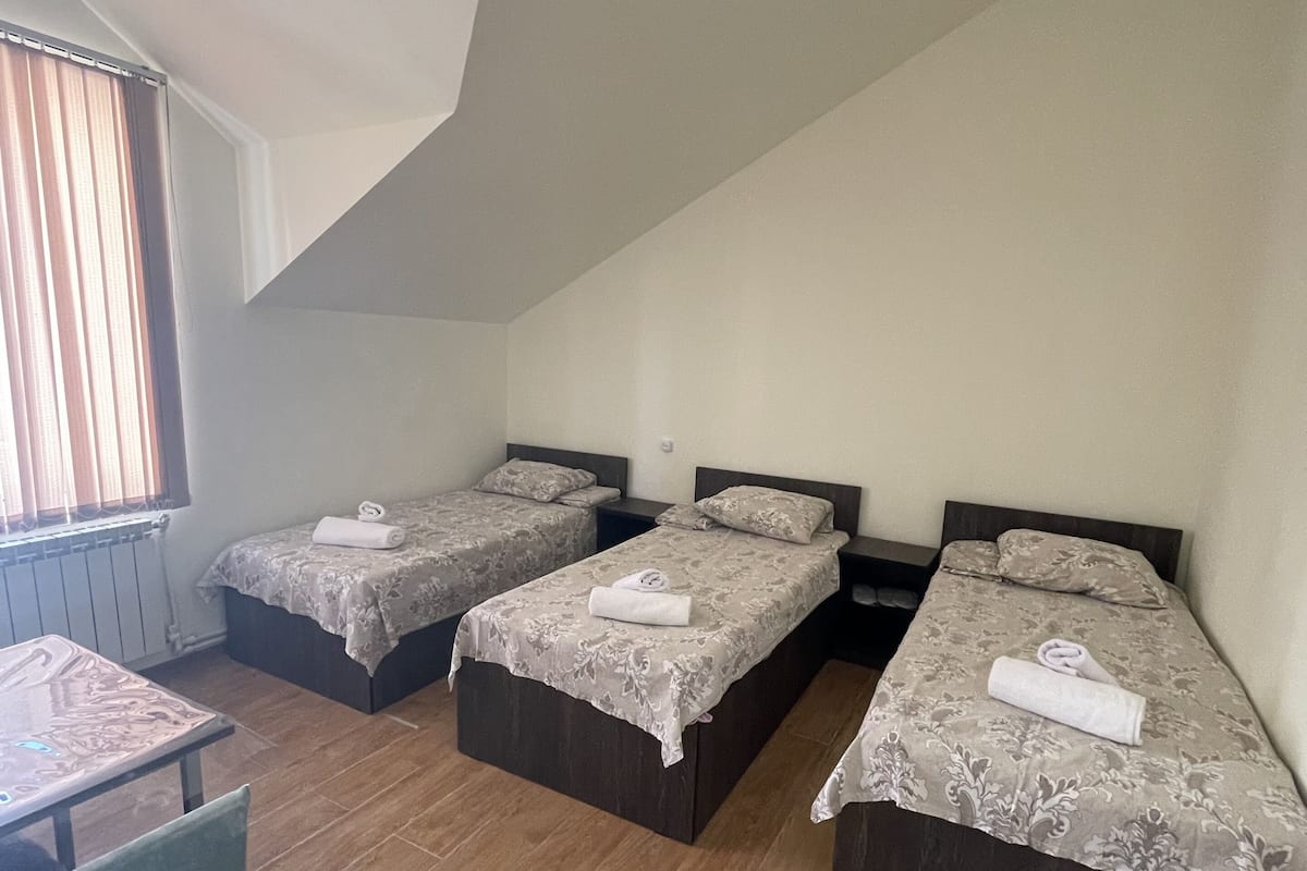 Une chambre de dortoir avec trois lits simples, une petite table et une chaise.