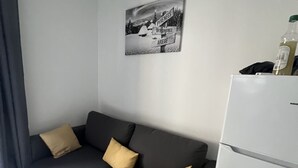 A modern living room with a grey sofa, two cushions, a black and white photograph on the wall, and a white refrigerator. - Ouréa, Appartement aux Portes de Ax les Thermes (Savignac-les-Ormeaux)