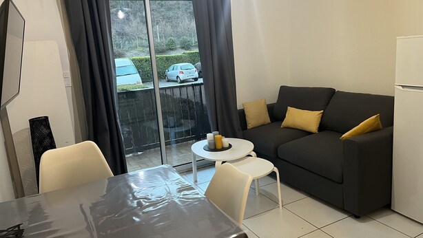 A compact living space with a sofa, a small round table, and a dining table. - Ouréa, Appartement aux Portes de Ax les Thermes (Savignac-les-Ormeaux)