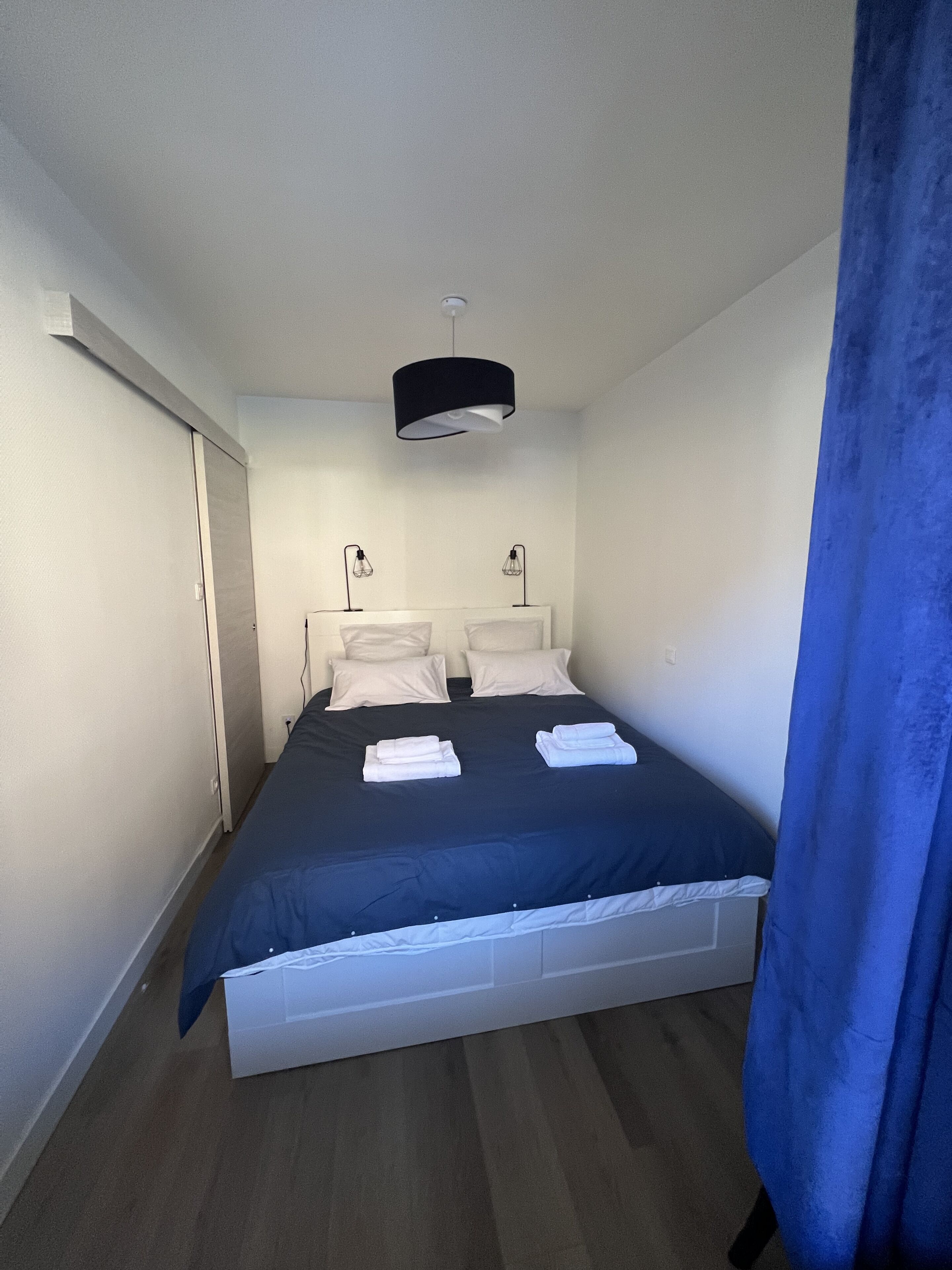 A bedroom with a bed, bedside lamps, a ceiling light, and a blue curtain.