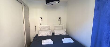 A bedroom with a bed, bedside lamps, a ceiling light, and a blue curtain.