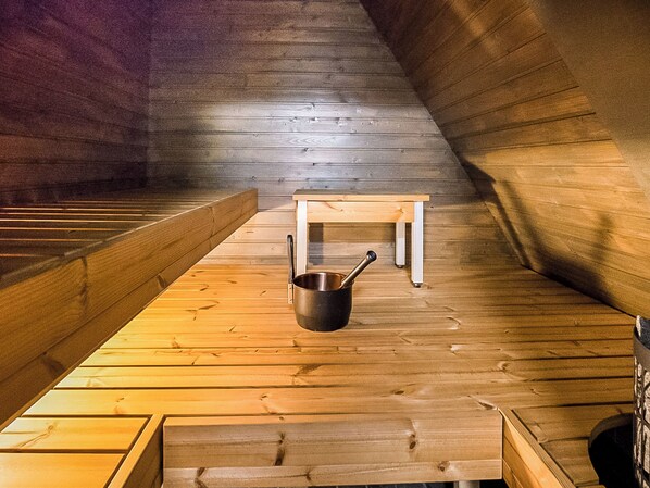 Un interior de madera con un banco, una mesa, una olla en el suelo y una ventana.