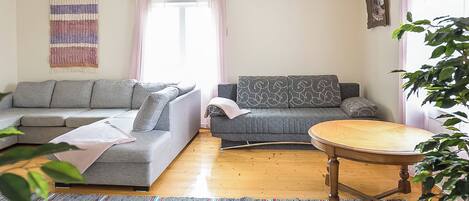 A living room with a sofa, a smaller couch, a round wooden table, and a patterned rug.