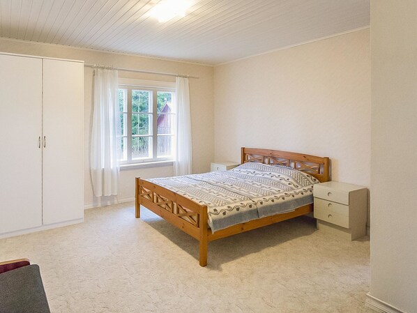 Une chambre à coucher avec un lit en bois, une table de chevet, une armoire et une fenêtre avec des rideaux.