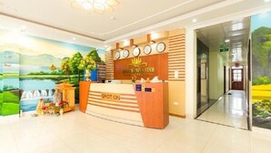 A hotel reception desk with a scenic mural, a clock, and a 'SPOT ON' sign. - Sunrise Ninh Binh Hotel (Hoa Lu)