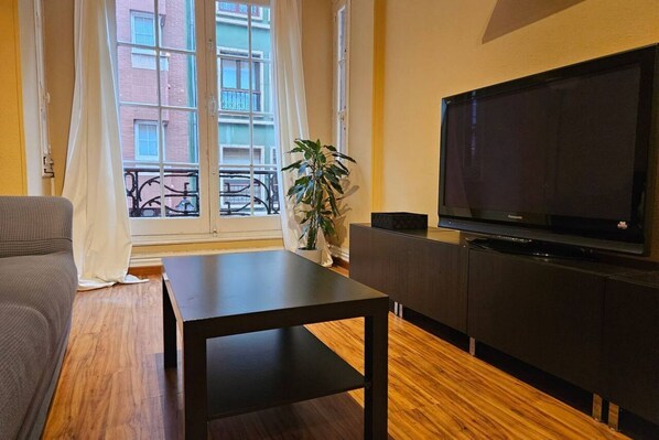 A living room with a sofa, a table, a TV, and a plant.