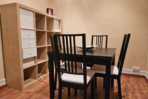 A dining area with a wooden table and four chairs, a wooden cabinet with open shelves, and a beige textured wall.