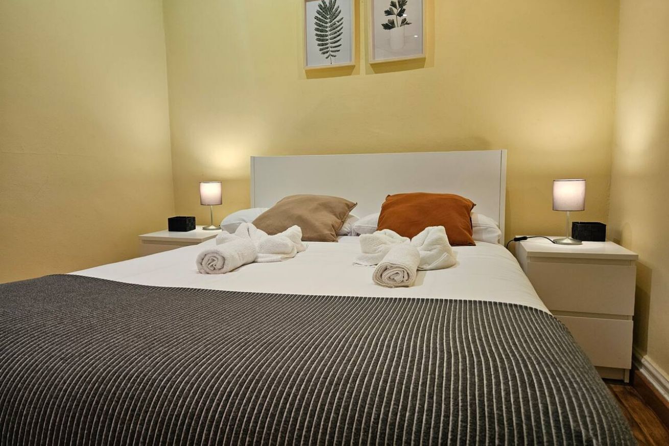 A neatly made bed with pillows, a striped blanket, and rolled towels on a white headboard.