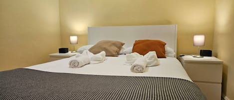 A neatly made bed with pillows, a striped blanket, and rolled towels on a white headboard.