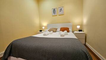 Habitación de hotel con una cama, dos mesitas de noche, un cabecero y dos cuadros en la pared.