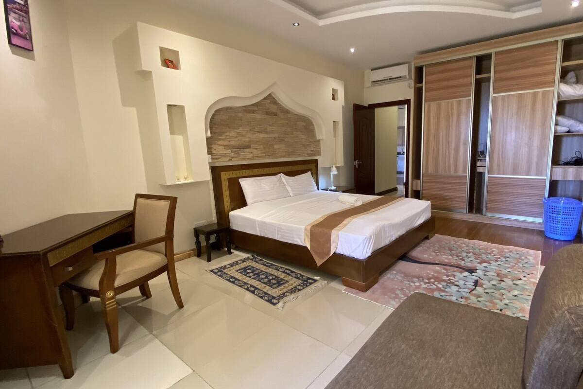 A bedroom with a bed, desk, chair, and wardrobe.